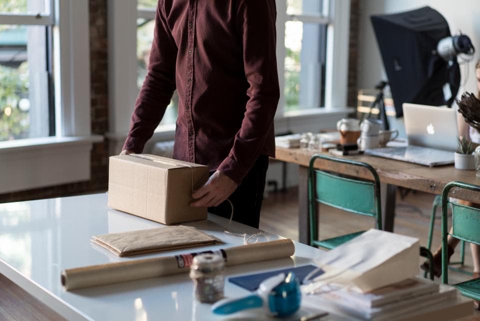 Personne tenant un carton d'expédition sur un bureau, avec du matériel d'emballage.