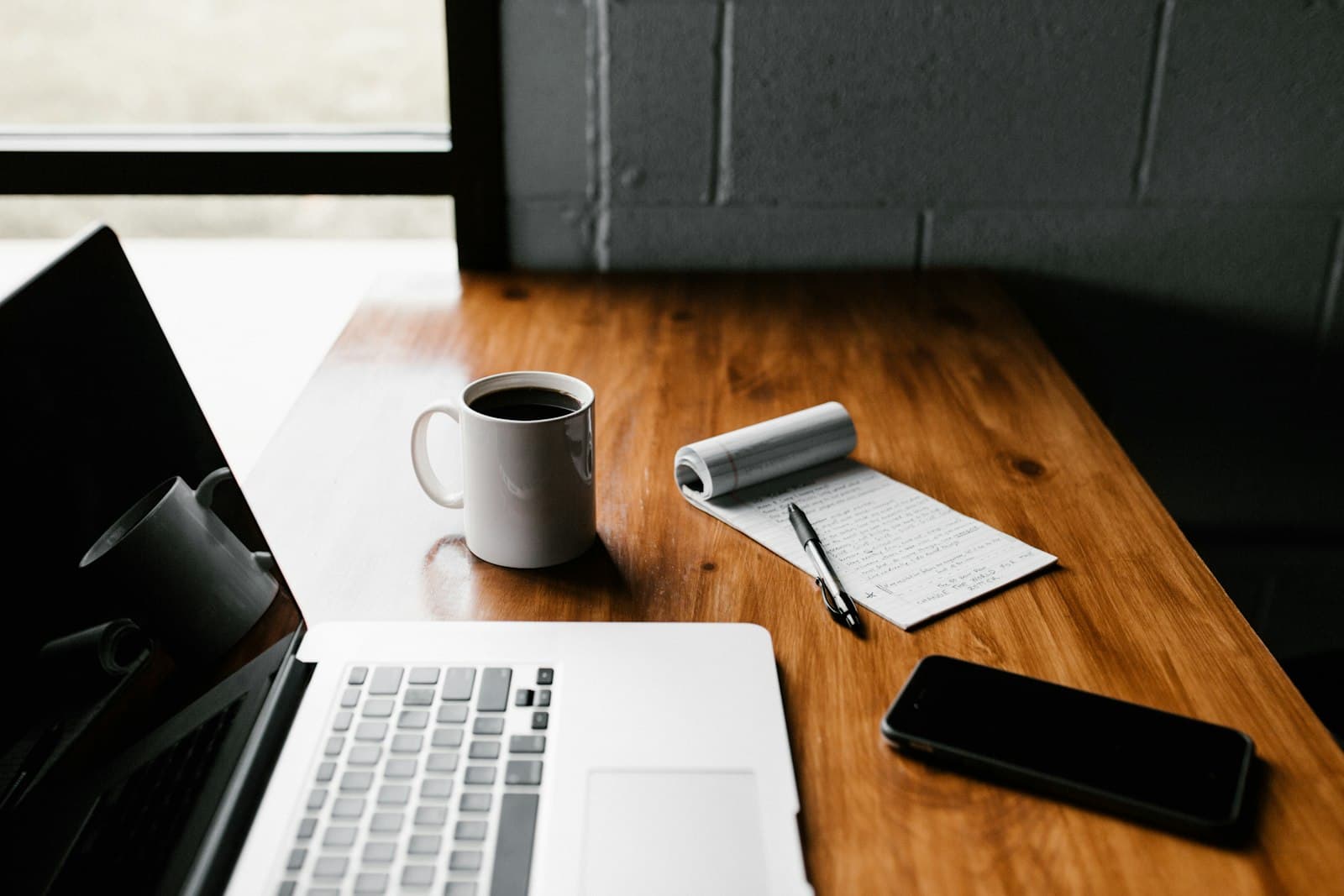 Tasse de café et carnet posés sur un bureau au petit matin, début de journée de travail.