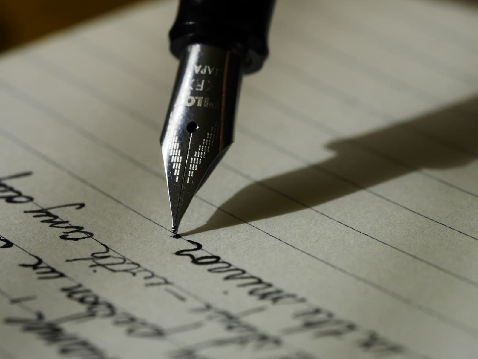 Plume d'un stylo écrivant à la main sur une feuille lignée.