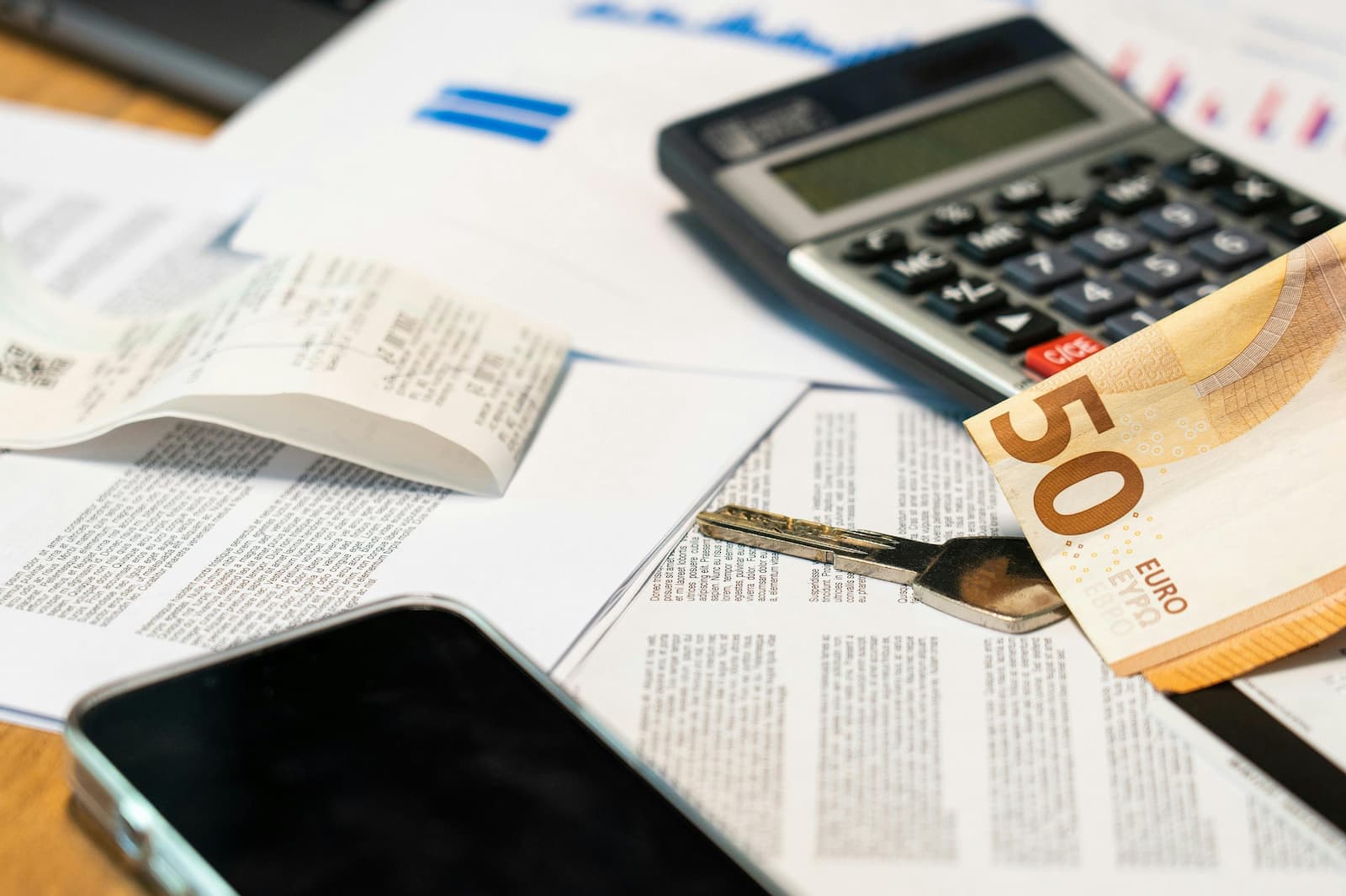 Bureau avec calculatrice, reçus papier, smartphone et billet de 50 euros : gestion comptable et facturation.