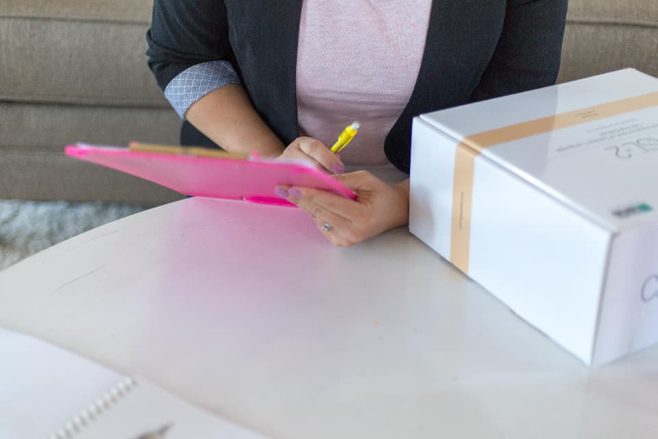 Main notant un inventaire sur une fiche, à côté d'un colis.